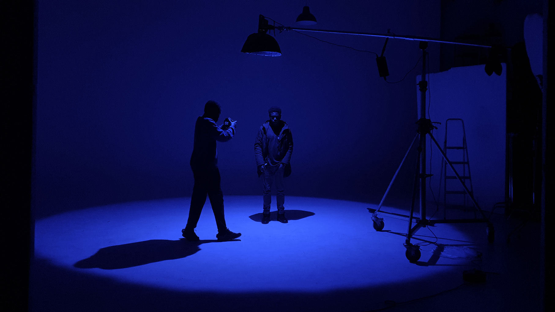 Camera operator filming a performer beneath a boomed light in a blue-lit infinity cove at Cineview Studios London