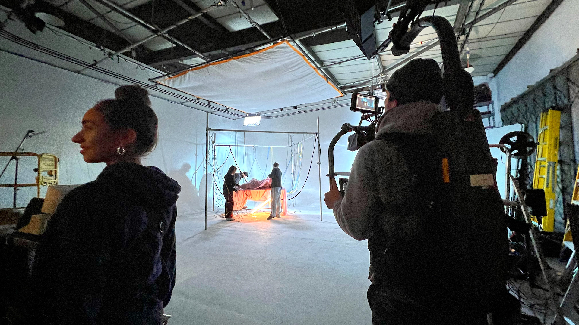 a camera man setting up his camera for a music video shoot at white infinity cove photography studio with large silk hanging on lighting grid