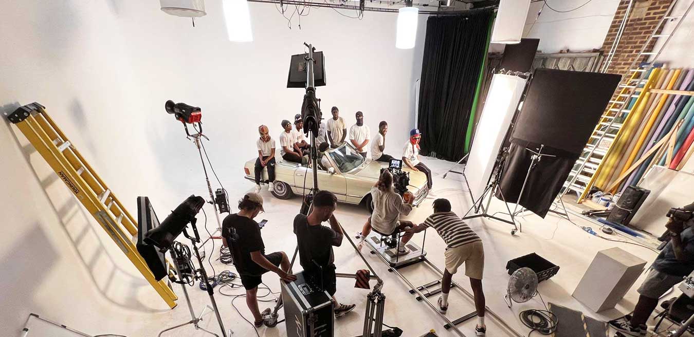A large film studio space where a dolly and track is setup with artist sitting on top of a car for music video shoot