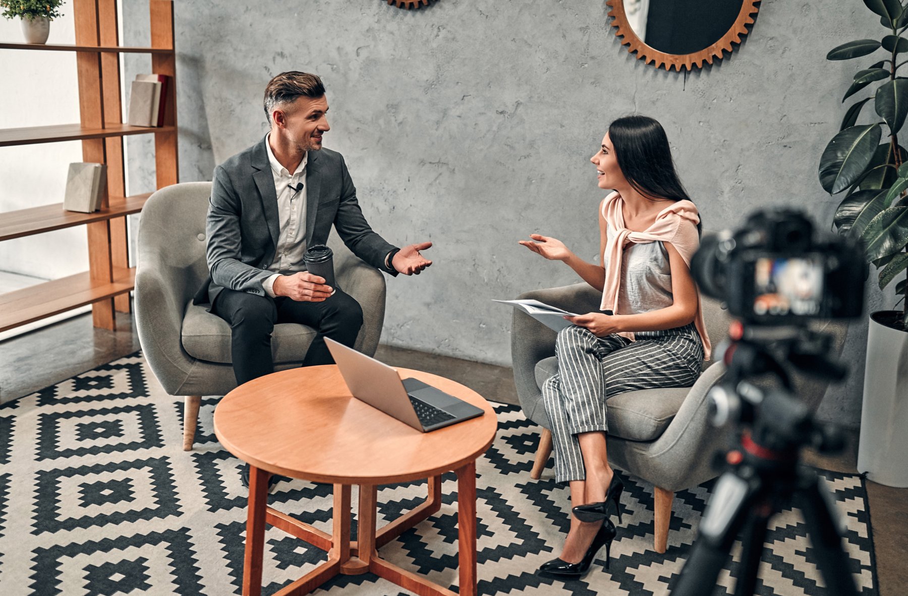 An interviewer speaking with a business guest while a camera records