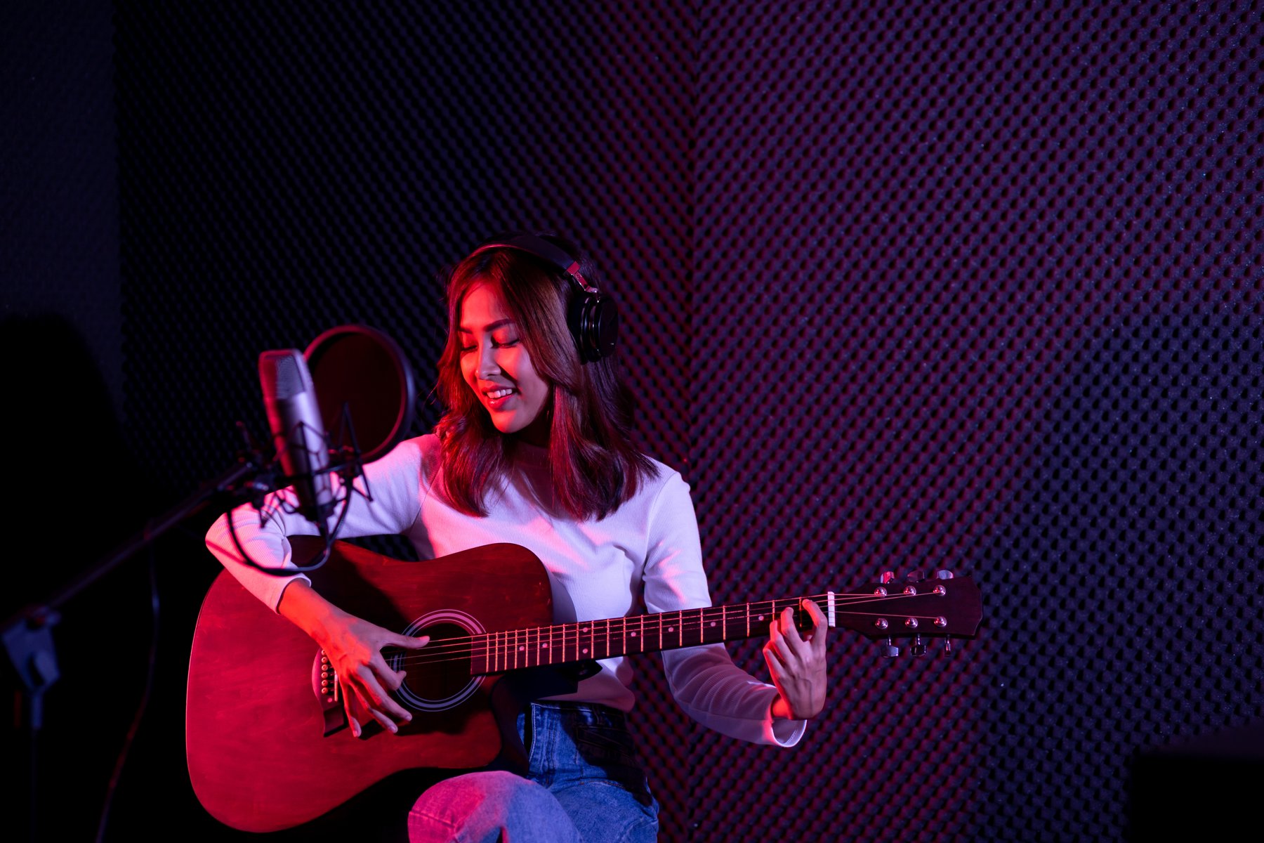 Singer playing acoustic guitar beside a recording microphone