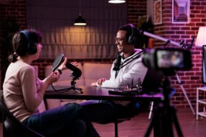 A camera recording two podcast guests speaking into microphones
