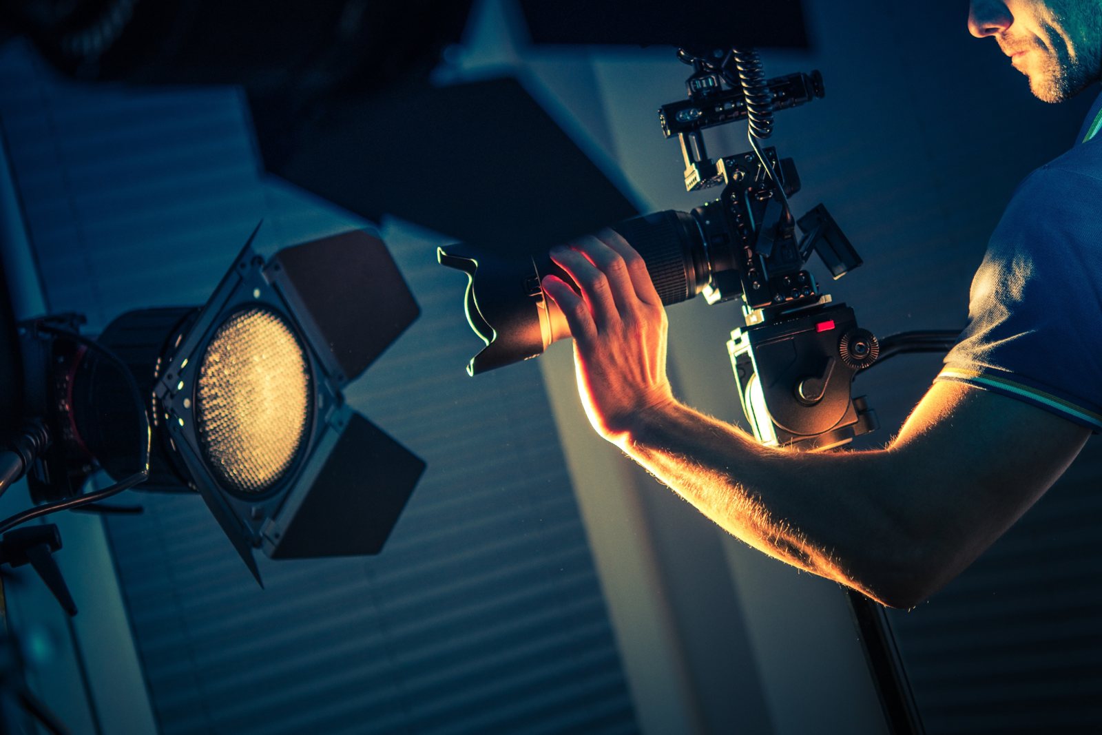 Camera operator adjusting a cinema camera beside a film light