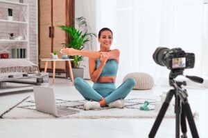 A camera recording a fitness presenter demonstrating a seated stretch