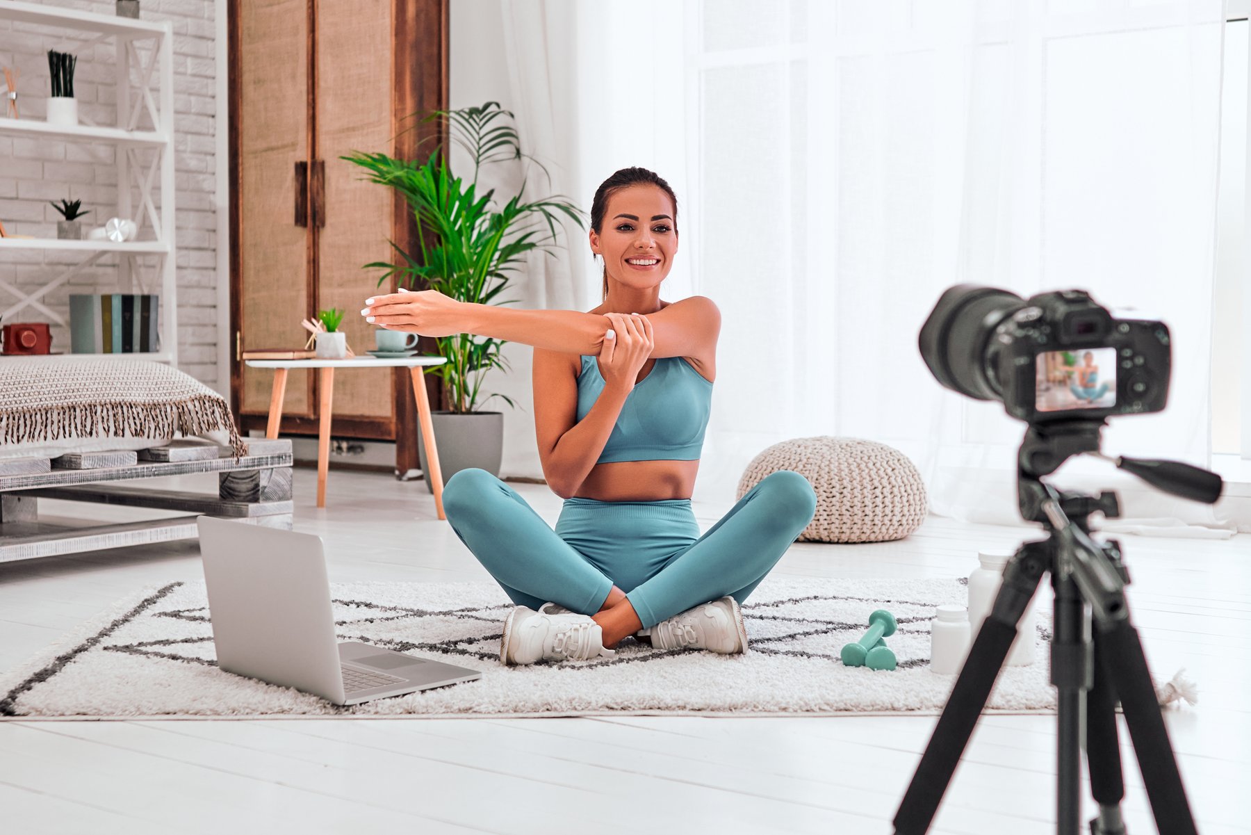 A camera recording a fitness presenter demonstrating a seated stretch