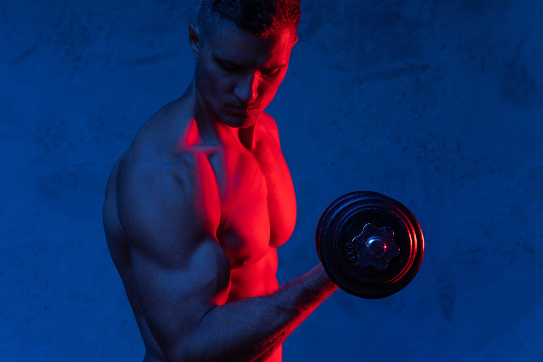 Fitness portrait with a dumbbell under blue and red studio lighting