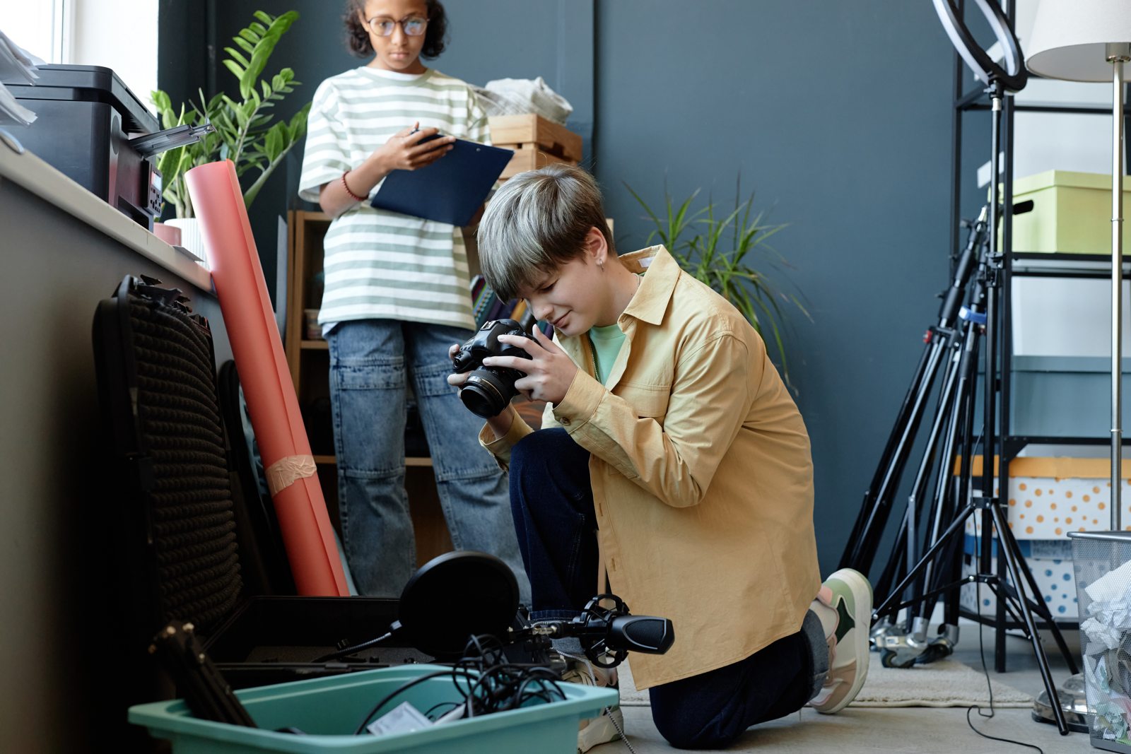 Young photographer setting up a camera while a colleague reviews a clipboard